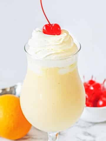 Orange shake topped with whip cream and cherry in a tall glass.