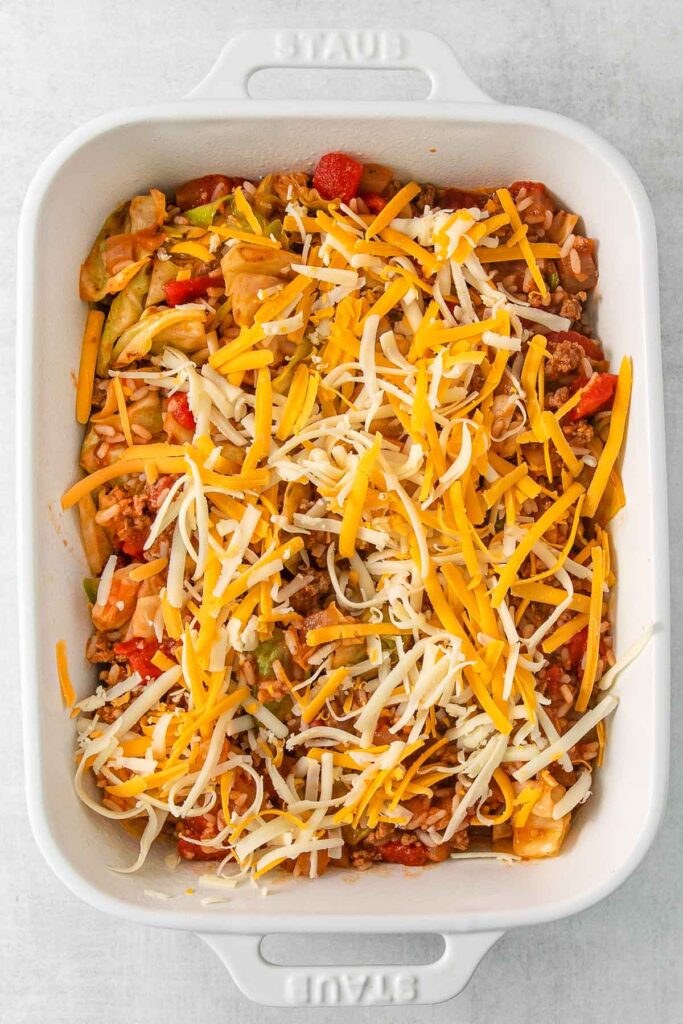 Cabbage roll casserole in a white baking dish with unmelted cheese.