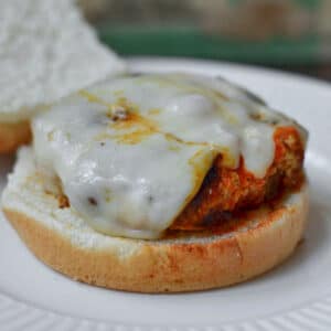 A close-up of a turkey burger with melted cheese on a bun on a white plate.