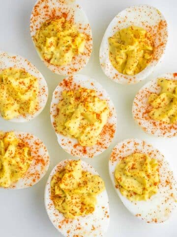 Several deviled eggs garnished with paprika arranged on a white plate.