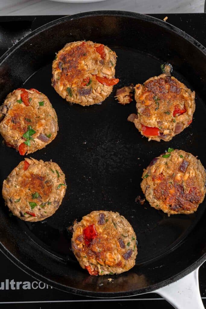 Salmon croquettes being cooked in a large skillet.