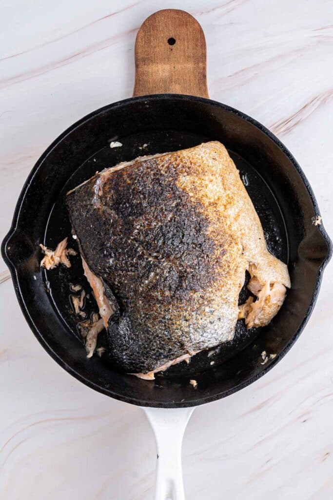 Cooked salmon fillet with crispy, seasoned skin, presented in a black cast iron skillet on a wooden serving board.