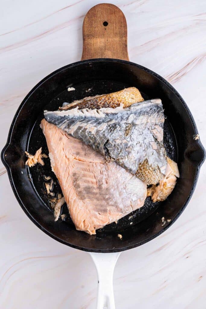 A cooked salmon fillet with crispy skin in a black cast iron skillet.
