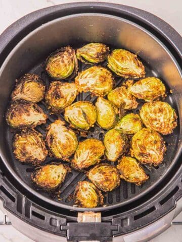 An air fryer on a metal rack containing slightly charred Brussels sprouts.