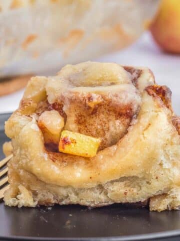 A single piece of apple cinnamon roll on a black plate with a fork.