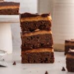 Three stacked chocolate placed on a counter, with additional brownies in the background.