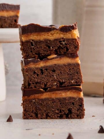 Three stacked chocolate placed on a counter, with additional brownies in the background.