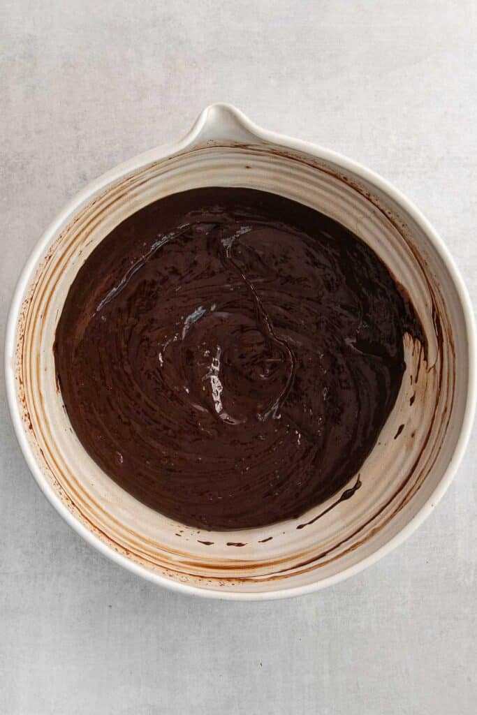 A white mixing bowl with chocolate batter mixed inside.