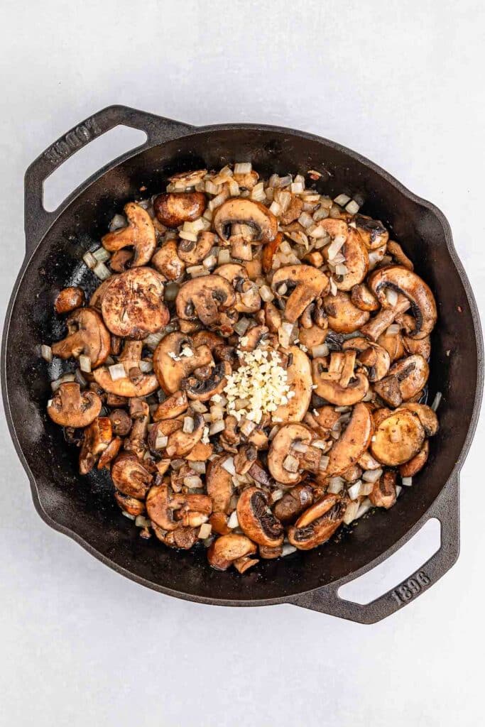 A cast iron skillet filled with cooked mushrooms, diced onions, and chopped garlic.