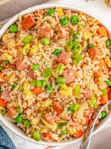 A white bowl of spam fried rice with a silver spoon on the side.