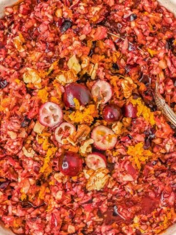 A bowl of cranberry relish with chopped walnuts, orange zest, and whole cranberries, with a spoon in the bowl.