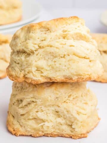 Two stacked, golden-brown homemade biscuits with flaky layers against a blurred background.