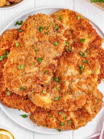 A plate of several golden-brown, breaded Milanesa steak garnished with parsley.