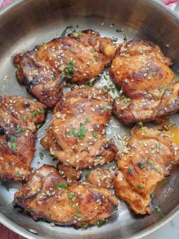 Cooked miso chicken thighs topped with sesame seeds and herbs in a skillet on a red and white checkered cloth.